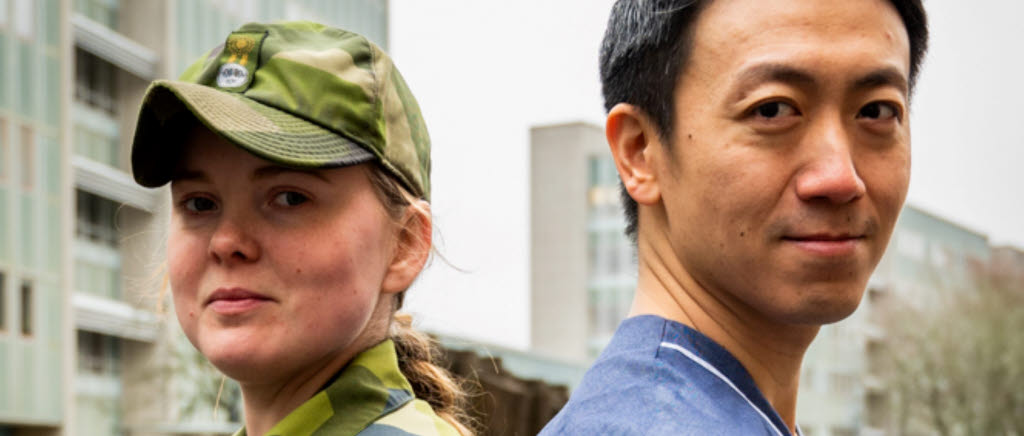 En kvinnlig soldat i grön uniform står rygg mot rygg med en manlig läkare i blå arbetskläder. Deras tygmärken och organisationsloggor syns på deras armar. 