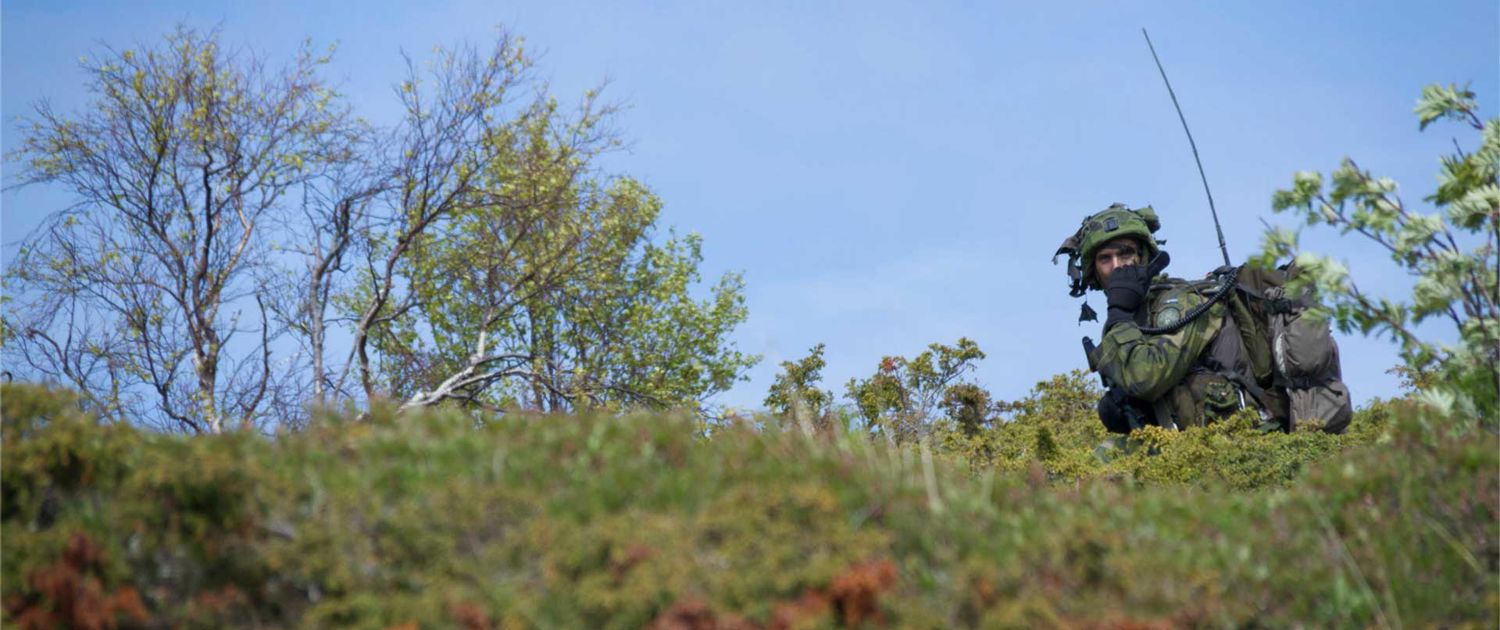 Militär med en telefon ute på fält.