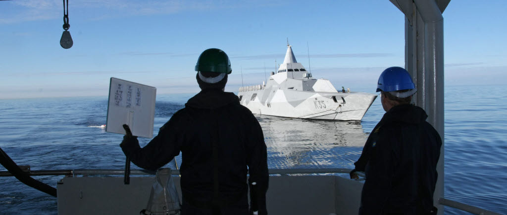 Med olikfärgade skyltar signalerar man mellan fartygen, det går snabbt och med liten risk för missförstånd.  I bakgrunden kustkorvetten HMS Härnösand (K35).