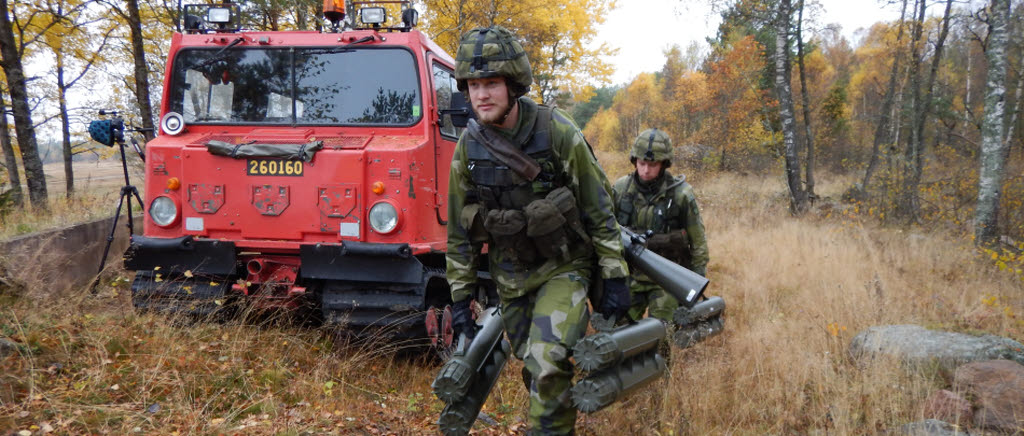 Två soldater går med sprängranat framför en röd bil i skogen