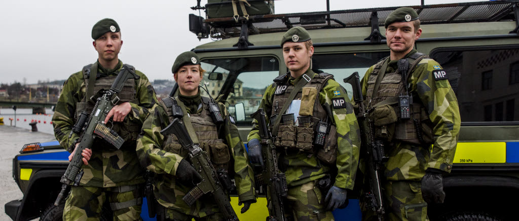 Militärpoliserna Adrian Blomqvist, Simone Schwartz, Harry Billefeldt och Erik Rinaldo står framför en av deras militärpolisbilar i Härnösand. De har stridsutrustning och basker på sig. Det svartvita MP-märket på deras vänstra arm kännetecknar att de är militärpoliser.