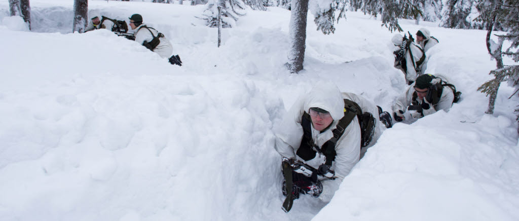 Kadetter i vita kamouflagekläder med vapen kryper i snön. 