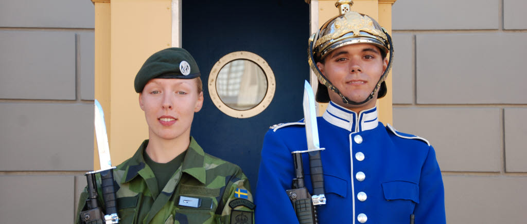 Två soldater står vid högvakten, den ena i m90 och den andra i högvaktens blåa uniform.