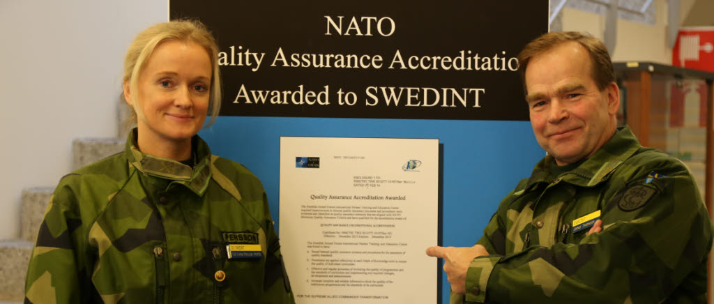 Överste Lena Persson Herlitz och överstelöjtnant Jerker Svensson står framför en plansch som visar att de nyss blivit ackrediterade av Nato. 