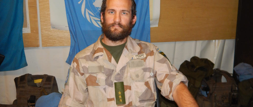Kapten Frans Eriksson sitter vid ett skrivbord framför FN-flagga. 