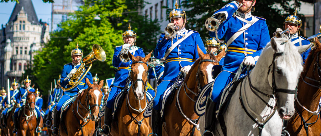 Beriden vaktparad med bruna och en vit häst. Soldaterna som rider har blå uniform.