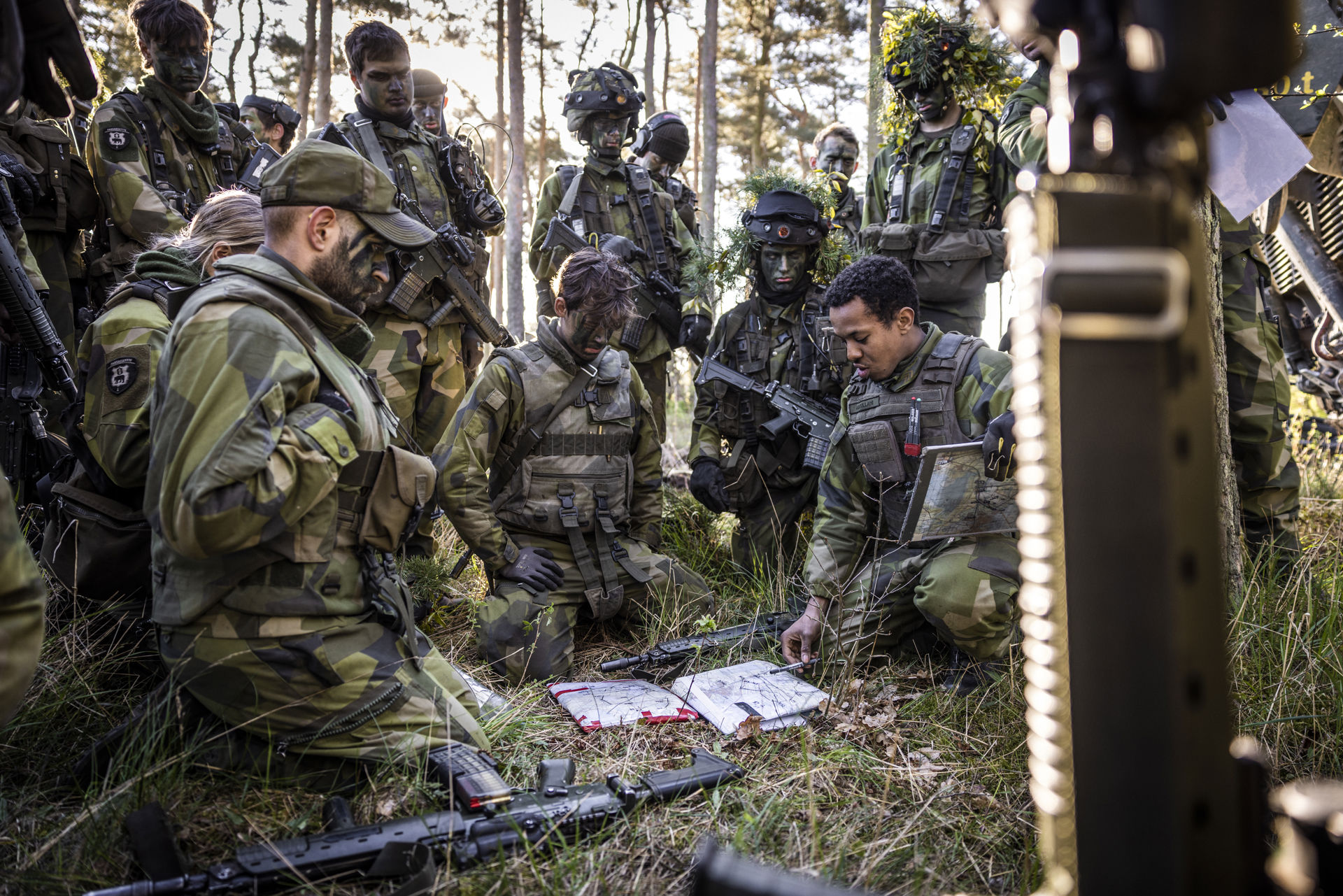 En grupp människor i uniform samlade kring en karta som ligger på marken i skogen.