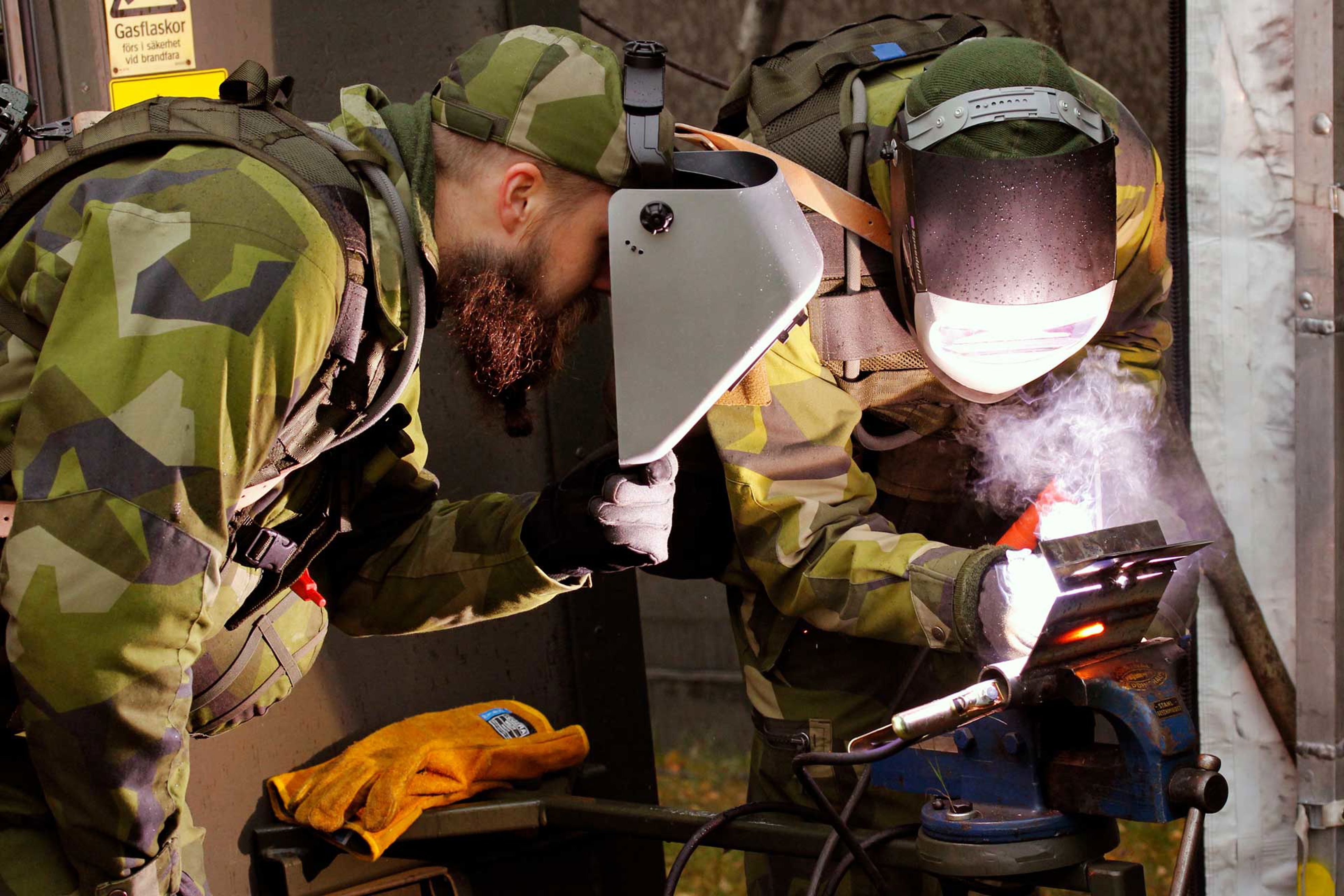 Två militärer utför en reparation i fält.