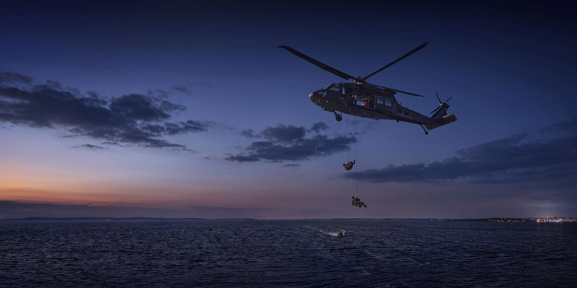 Två soldater som hänger med rep från en helikopter över havet.